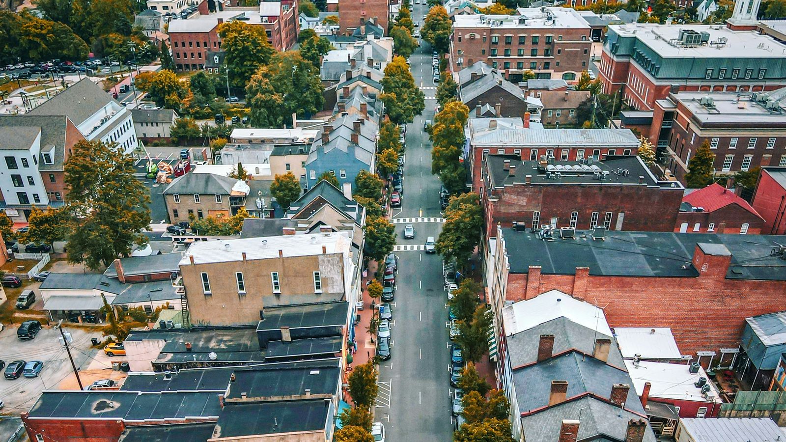 Aerial view of a small-town main street lined with brick storefronts, trees, and sidewalk seating